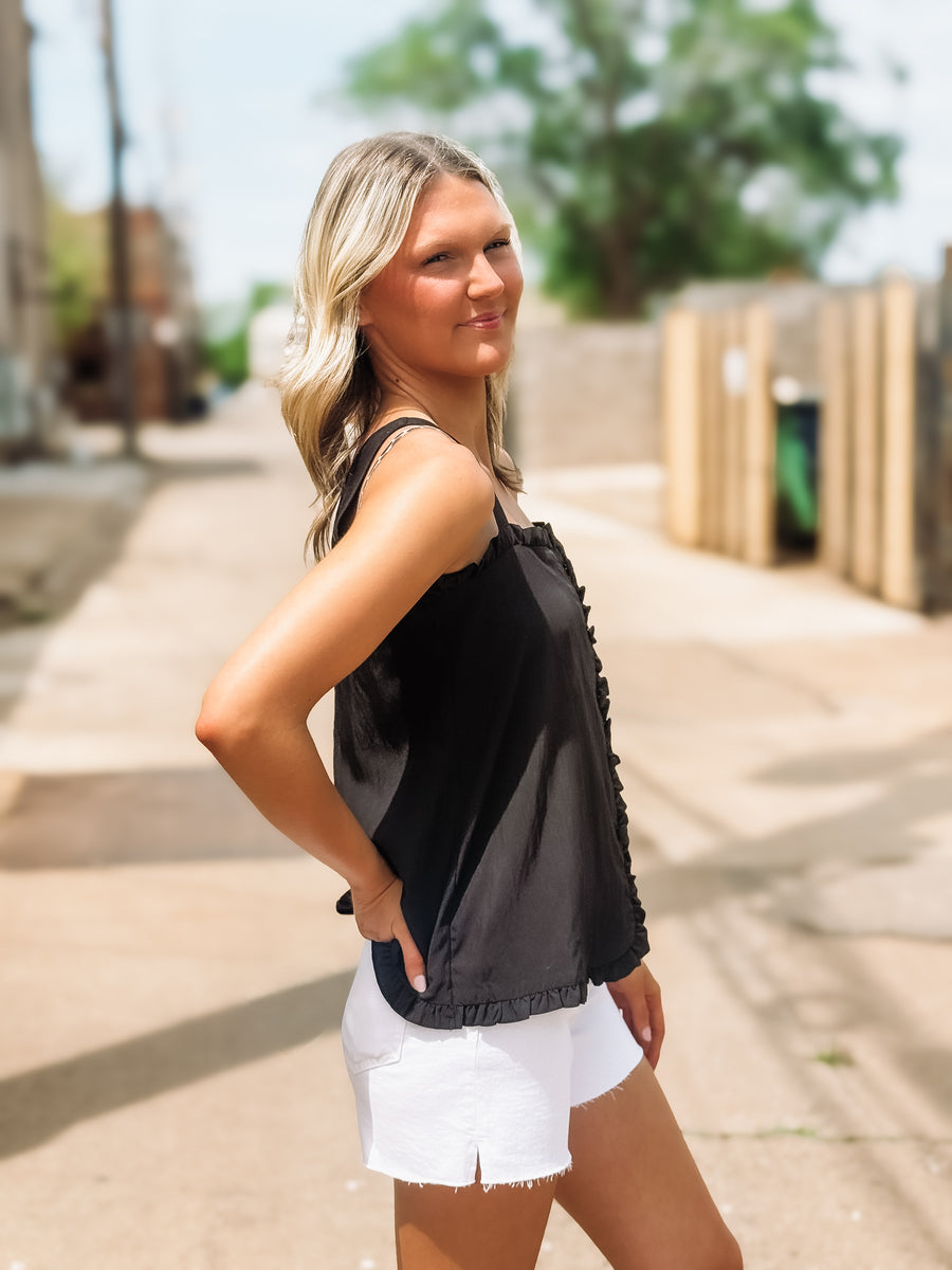 Woman wearing a black sleeveless top and white shorts standing on a sidewalk.