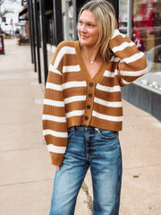 Woman wearing a brown and white striped sweater with blue jeans on a sidewalk.