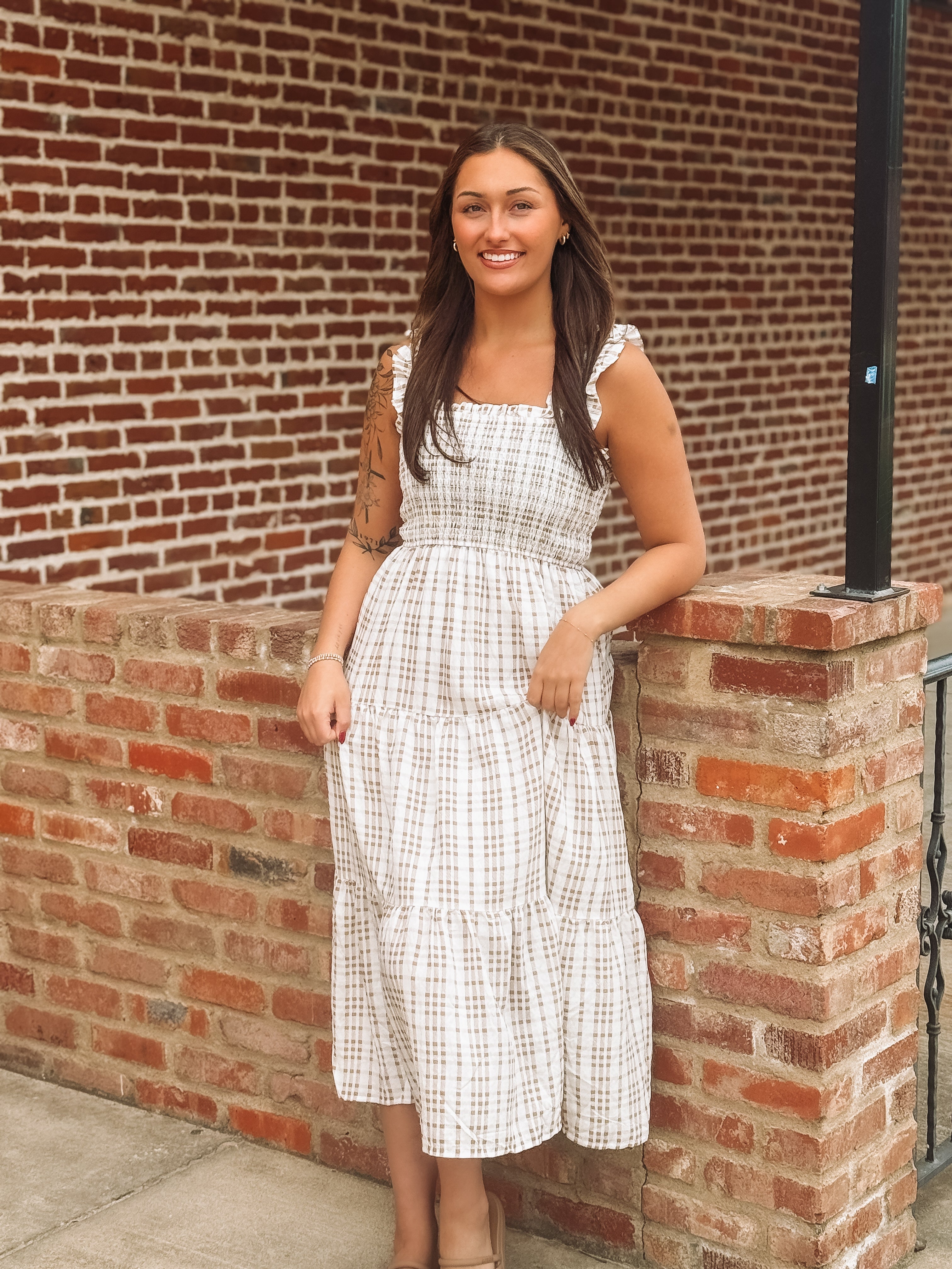 Woman in a brown and white dress standing against a brick wall