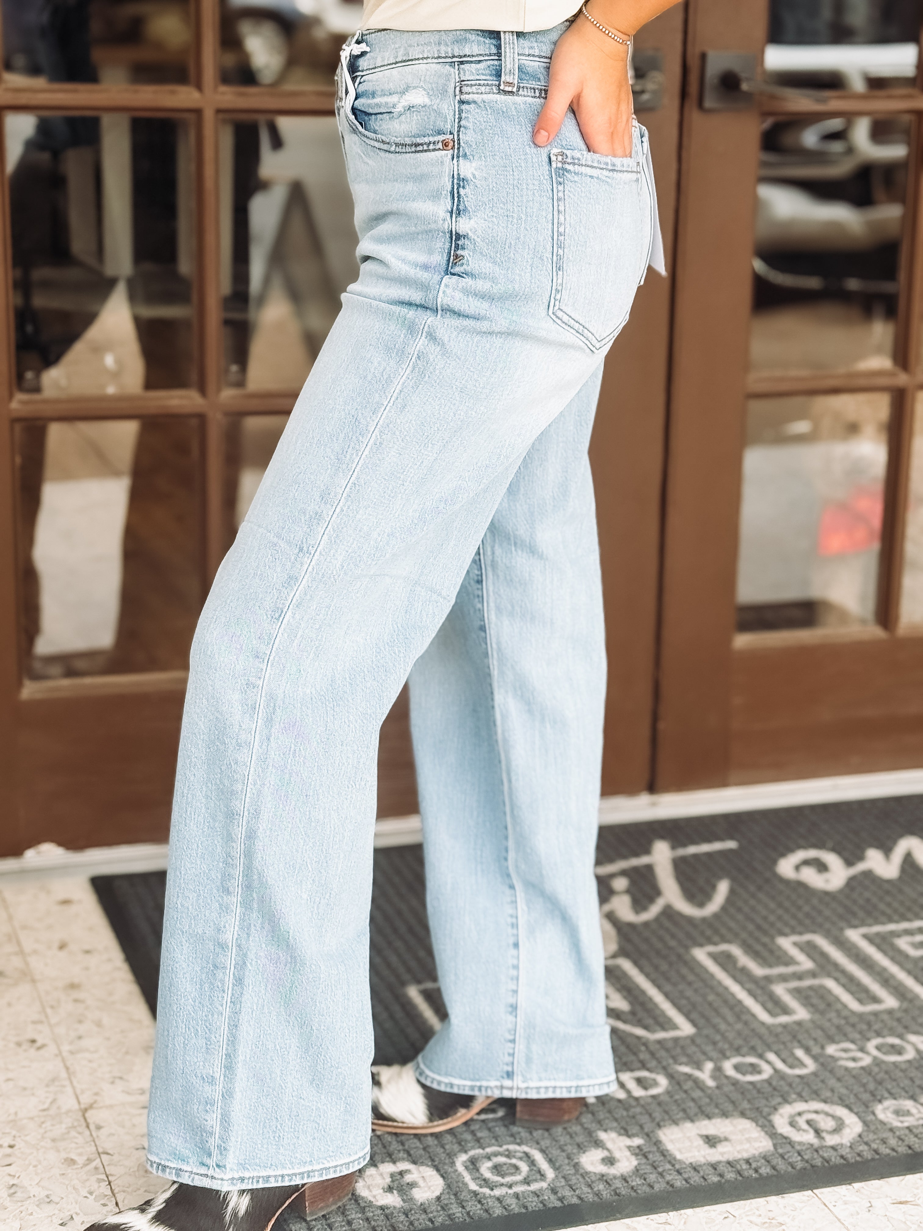 Light blue jeans worn by a person on a doormat with text.