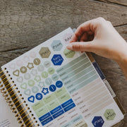 Hand placing decorative stickers on a planner with a wooden surface background