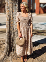 Woman in a polka dot dress holding a straw bag next to a tree