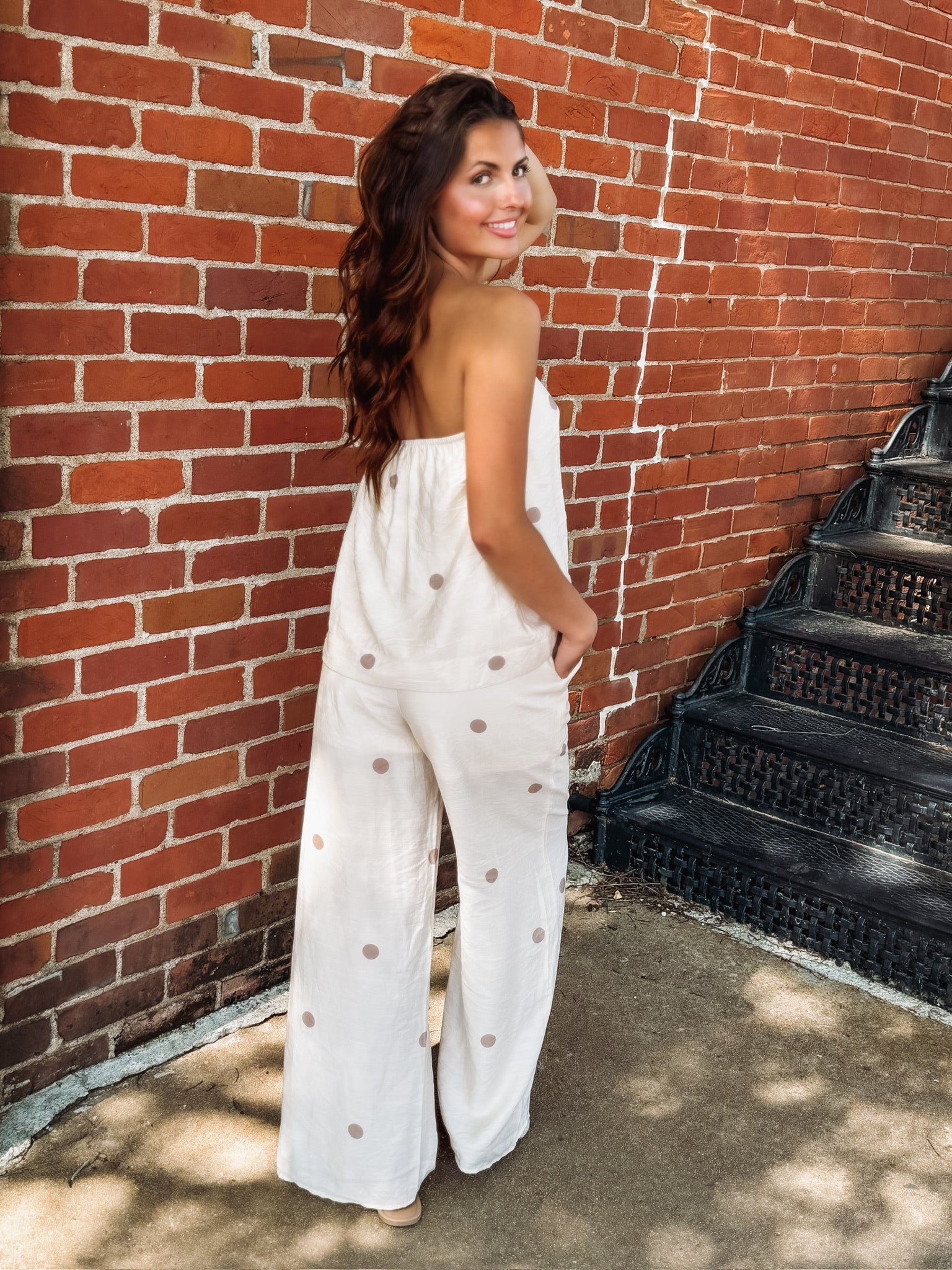 Strapless ecru matching pant  set featuring a flowy tube top with an elastic neckline and wide leg pants with an elastic drawstring waistband, pockets, and a soft light brown polka dot print.