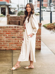 Loose, ankle length cream dress with three quarter puff sleeves and a split neckline. The dress features bold red floral embroidery with green stems arranged vertically down the front. It has a relaxed, flowy silhouette with side slits at the hem. 