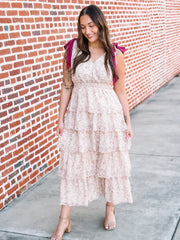 Woman in a floral dress standing against a brick wall.