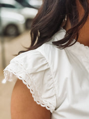 Close-up of a person wearing a white blouse with lace trim in an outdoor setting.