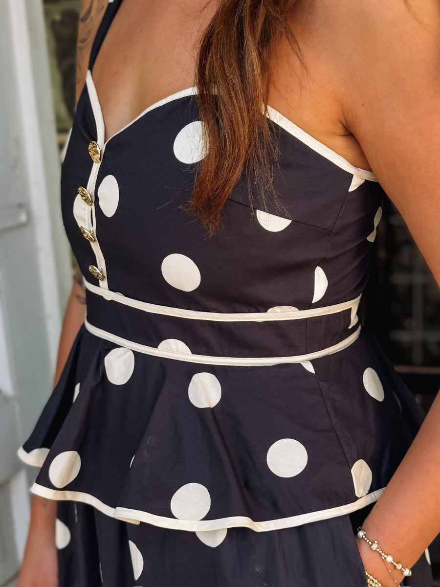 Black and white polka dot maxi dress with spaghetti straps, a tiered silhouette, and faux gold button details.
