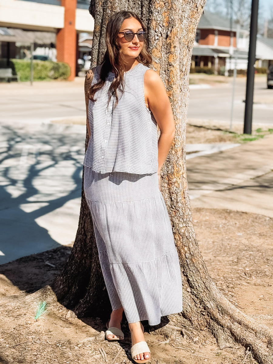 Woman in a sleeveless dress leaning against a tree on a street.