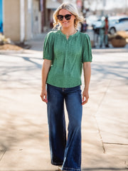 Woman wearing a green blouse and blue jeans on a street.