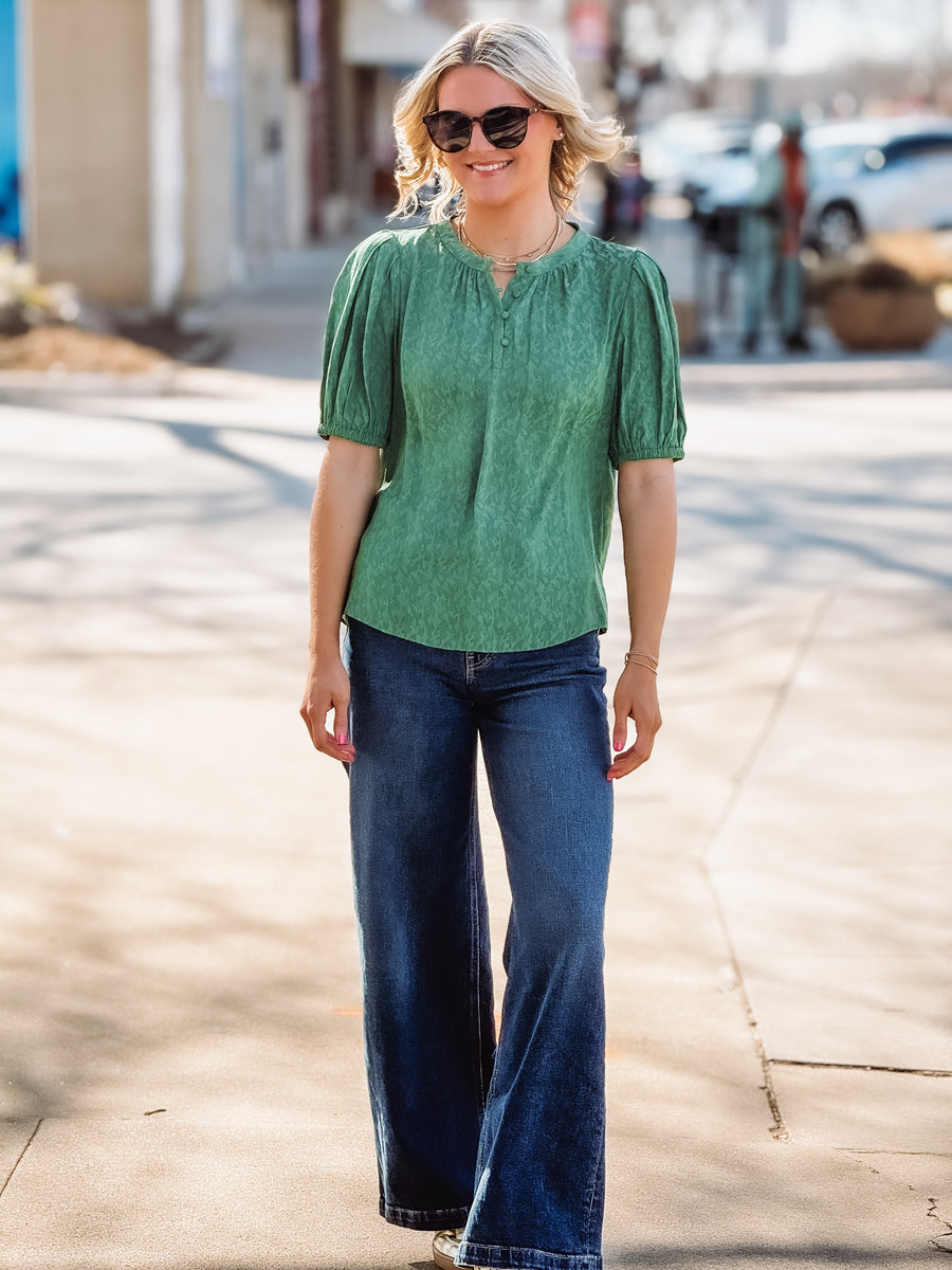 Woman wearing a green blouse and blue jeans on a street.