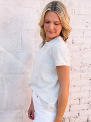 Woman wearing a light blue shirt and white pants against a textured white wall.