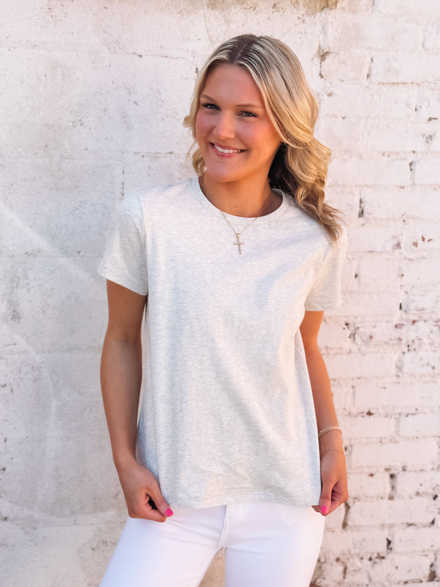 Woman wearing a light gray t-shirt and white pants against a textured white wall.