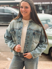 Woman wearing a denim jacket and jeans standing outdoors with blurred background