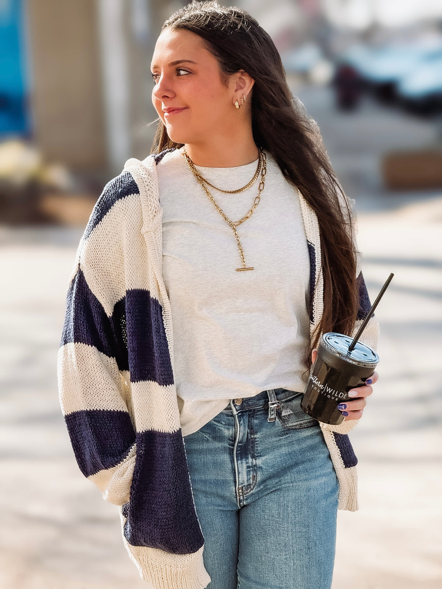 Woman holding a drink and wearing a striped cardigan on a street.