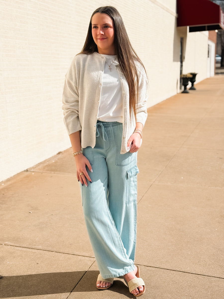 Woman wearing a light-colored cardigan, white shirt, and light blue pants on a sidewalk.