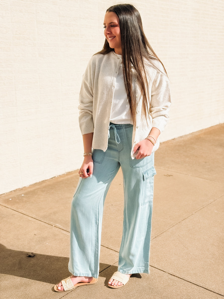 Woman wearing light blue cargo pants and a beige cardigan on a sidewalk.