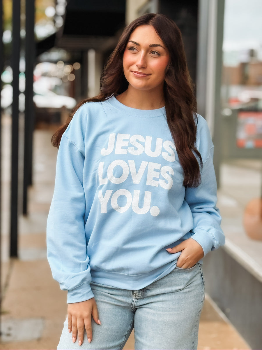 light blue crewneck sweatshirt with bold white text that reads ‘Jesus Loves You,’