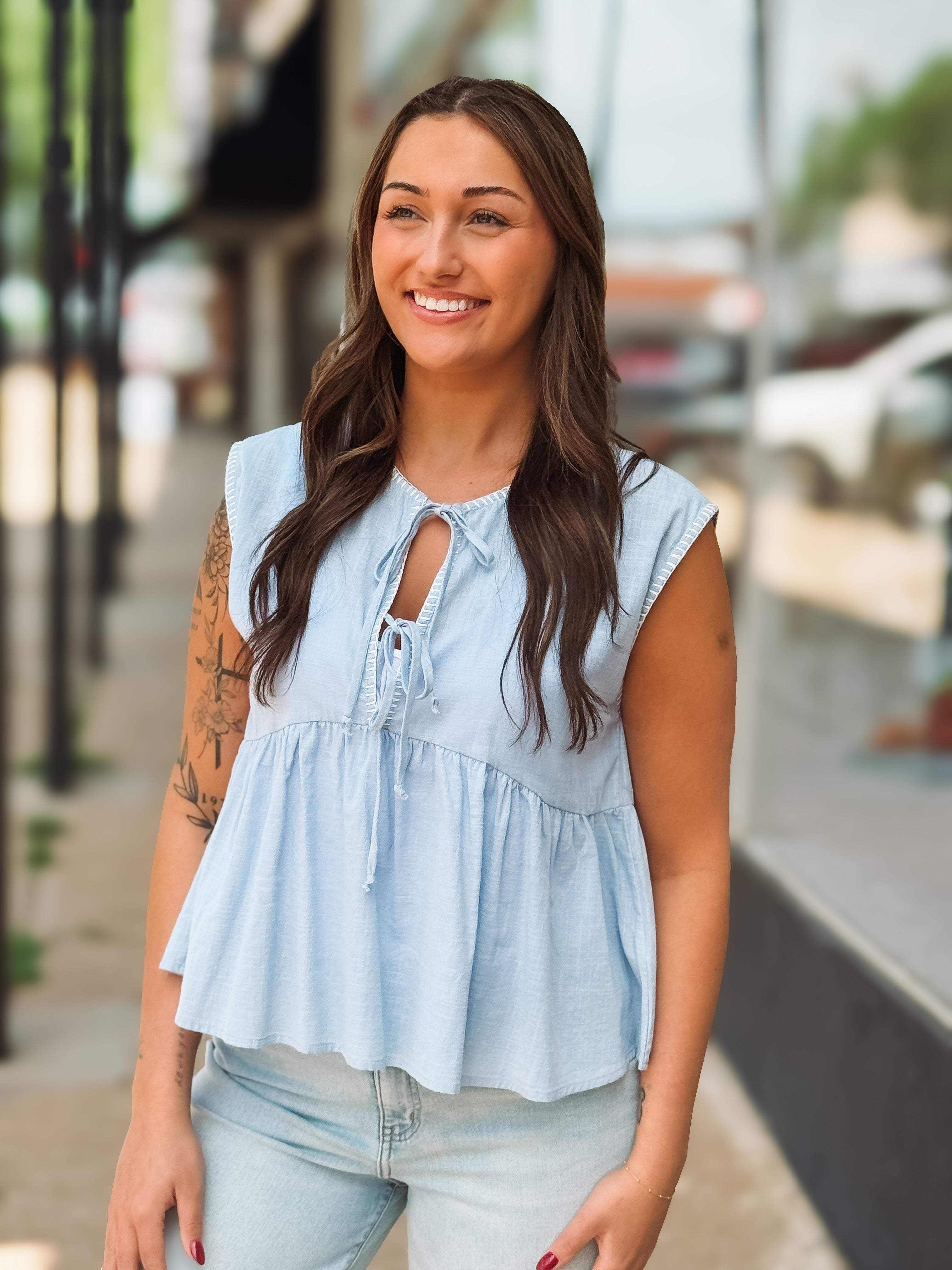 Woman wearing a light blue sleeveless top with a blurred background
