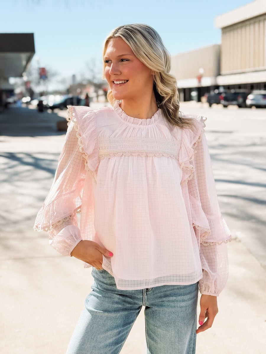 Woman wearing a light pink blouse with ruffled sleeves in an outdoor setting.
