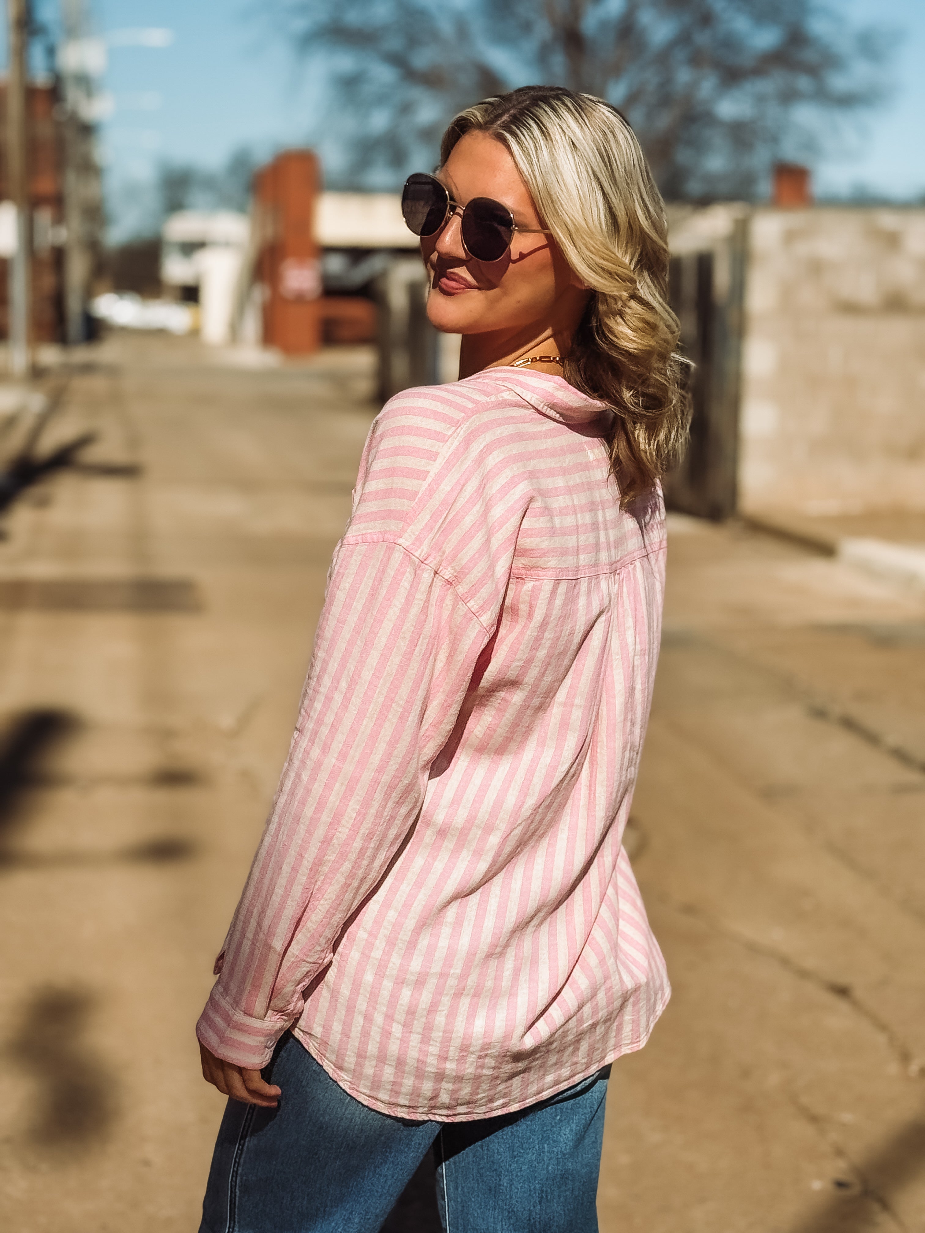 Woman wearing a pink striped shirt and sunglasses on a street.