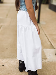 Person wearing a white skirt with a denim top on a sidewalk.