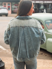 Person wearing a denim jacket standing in front of vintage cars.
