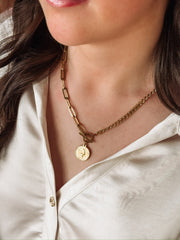Gold mixed chain necklace with a toggle closure and a small coin pendant.