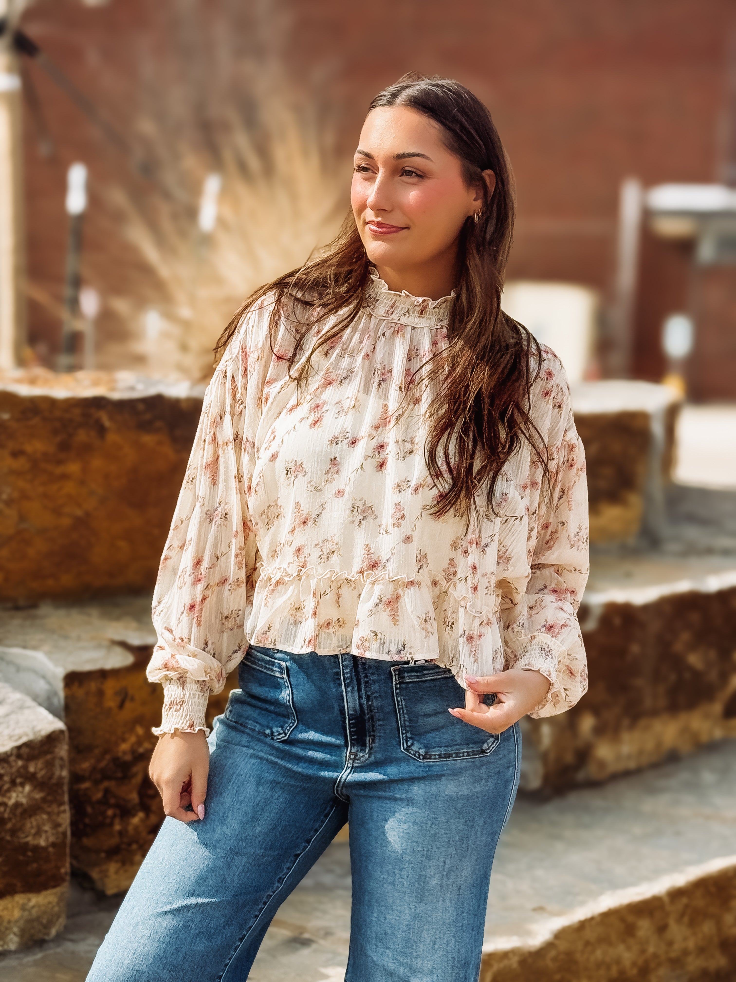 Woman wearing a floral blouse and blue jeans standing outdoors.