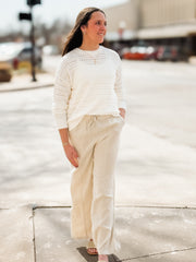 Woman wearing a white crochet sweater and beige pants on a city street.