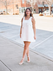 Woman in a white dress standing on a sidewalk with buildings in the background