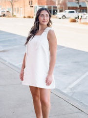 Woman in a white dress standing on a sidewalk with a blurred background