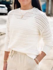 Person wearing a white crochet sweater with blurred background