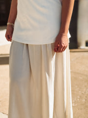 Person wearing a white sleeveless top and beige wide-leg pants against a neutral background