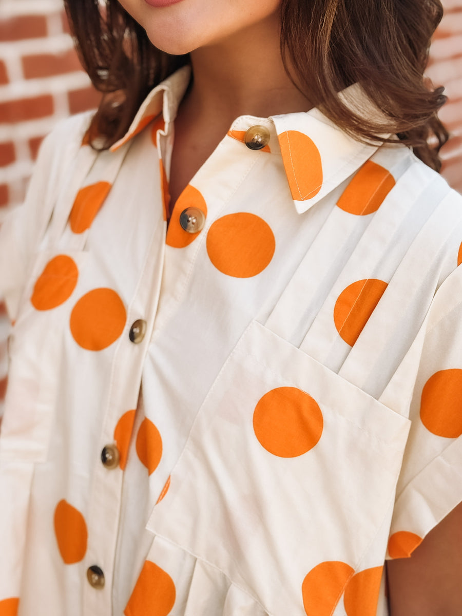 Cream mini dress with an orange polka dot print, button front closure, short sleeves, side pockets, and a relaxed fit.