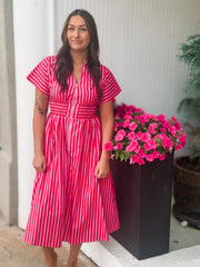 Woman in a pink and red striped dress standing next to a potted plant with pink flowers.