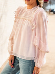 Woman wearing a light pink blouse with lace details and blue jeans.