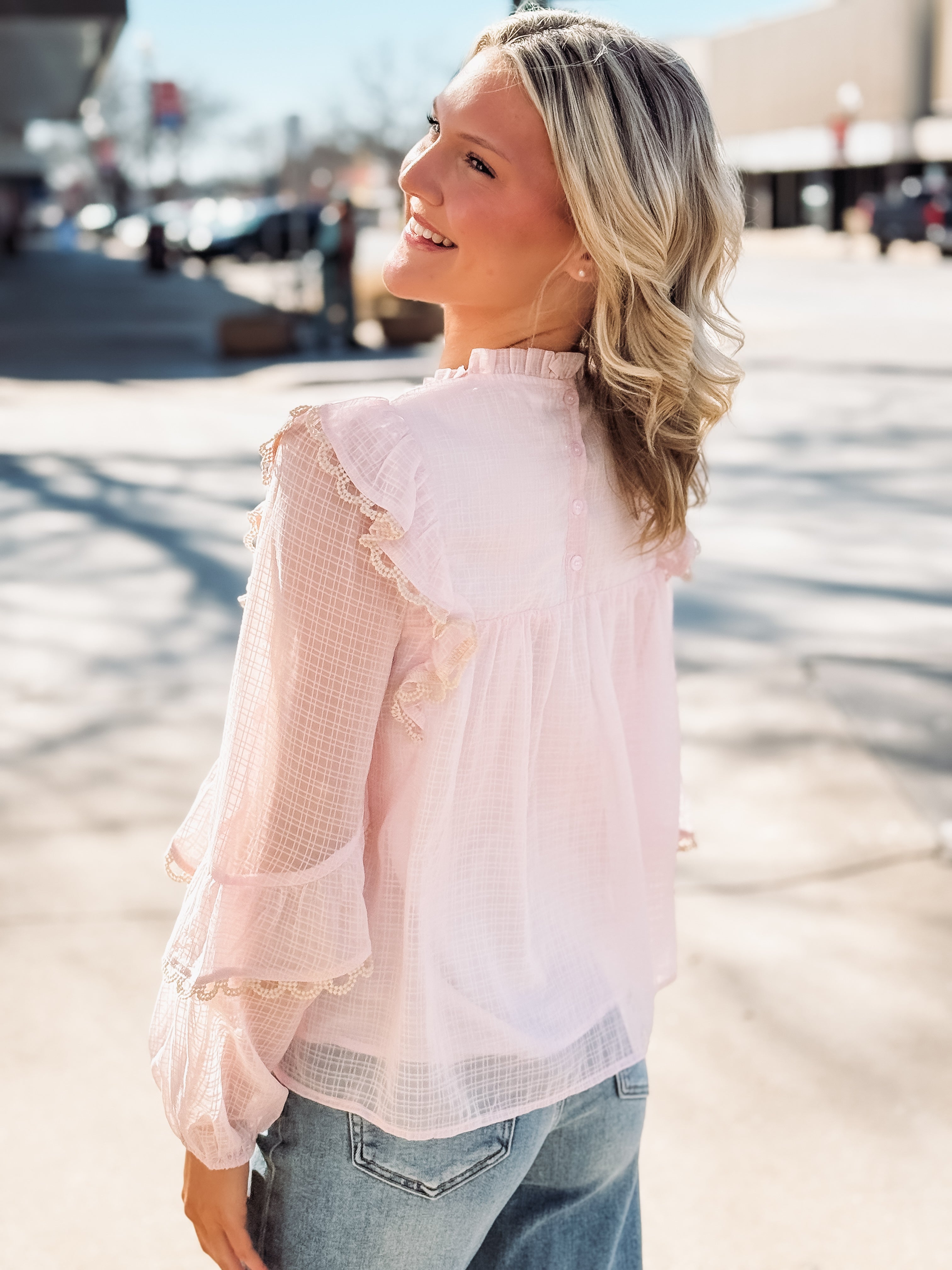Woman wearing a light pink blouse with ruffled details outdoors.