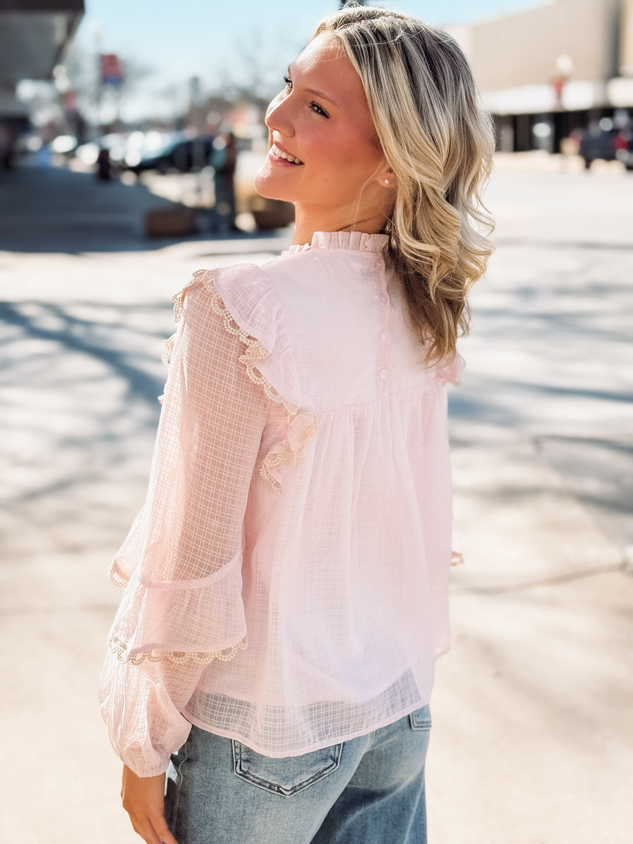 Woman wearing a light pink blouse with ruffled details outdoors.