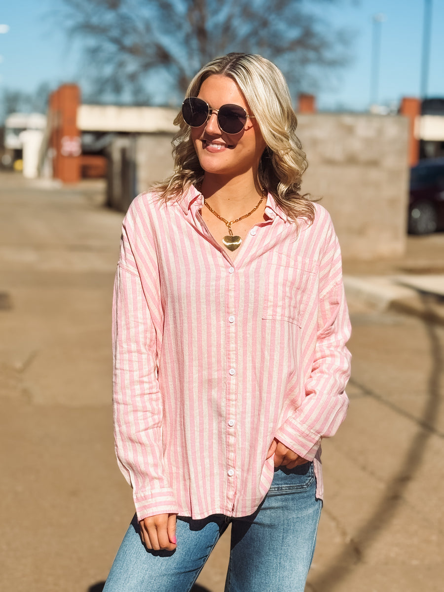 Woman wearing a pink striped shirt and sunglasses outdoors.