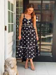 Black and white polka dot maxi dress with spaghetti straps, a tiered silhouette, and faux gold button details.
