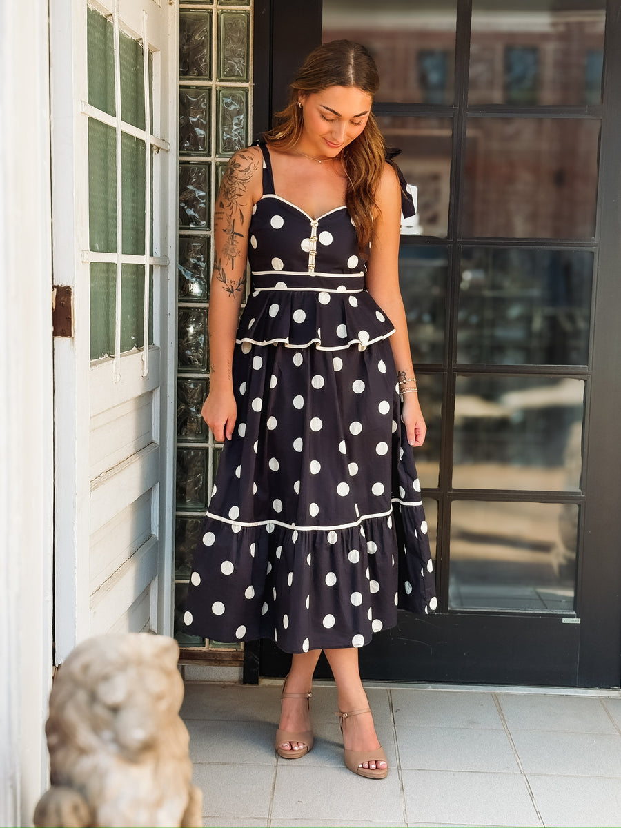 Black and white polka dot maxi dress with spaghetti straps, a tiered silhouette, and faux gold button details.

