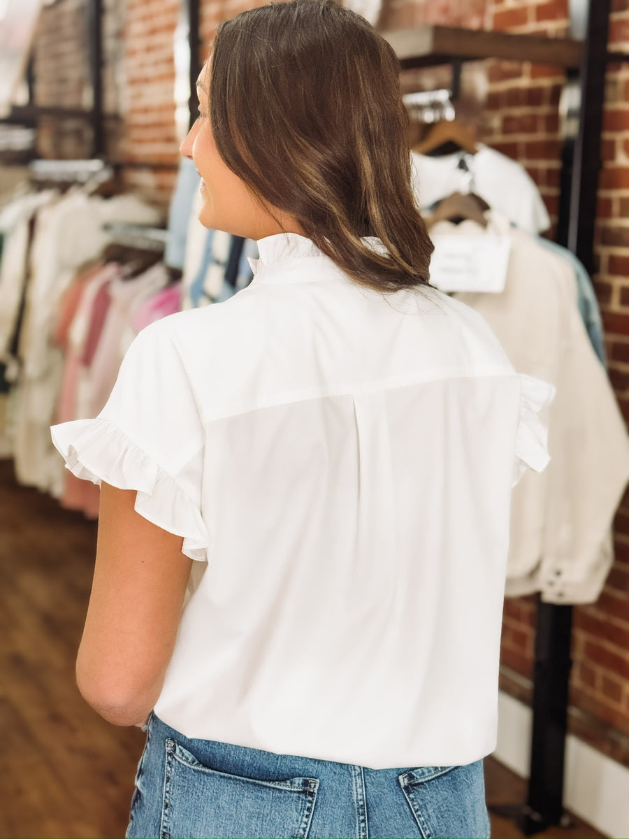 All white button up short sleeve blouse with ruffle detail on sleeves and mock neckline, featuring a full button up front.