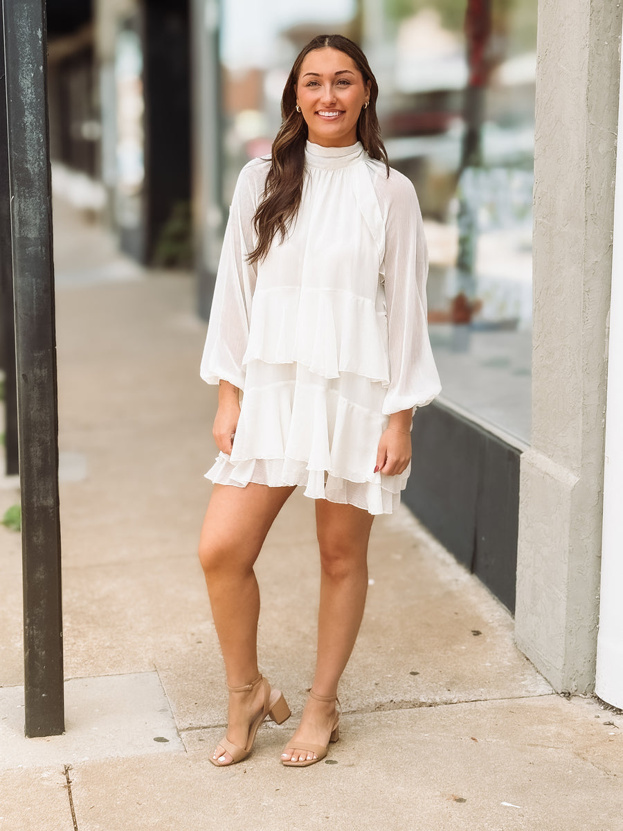 Woman wearing a white dress standing on a sidewalk.