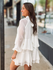 Woman wearing a white dress with ruffled layers on a city street.