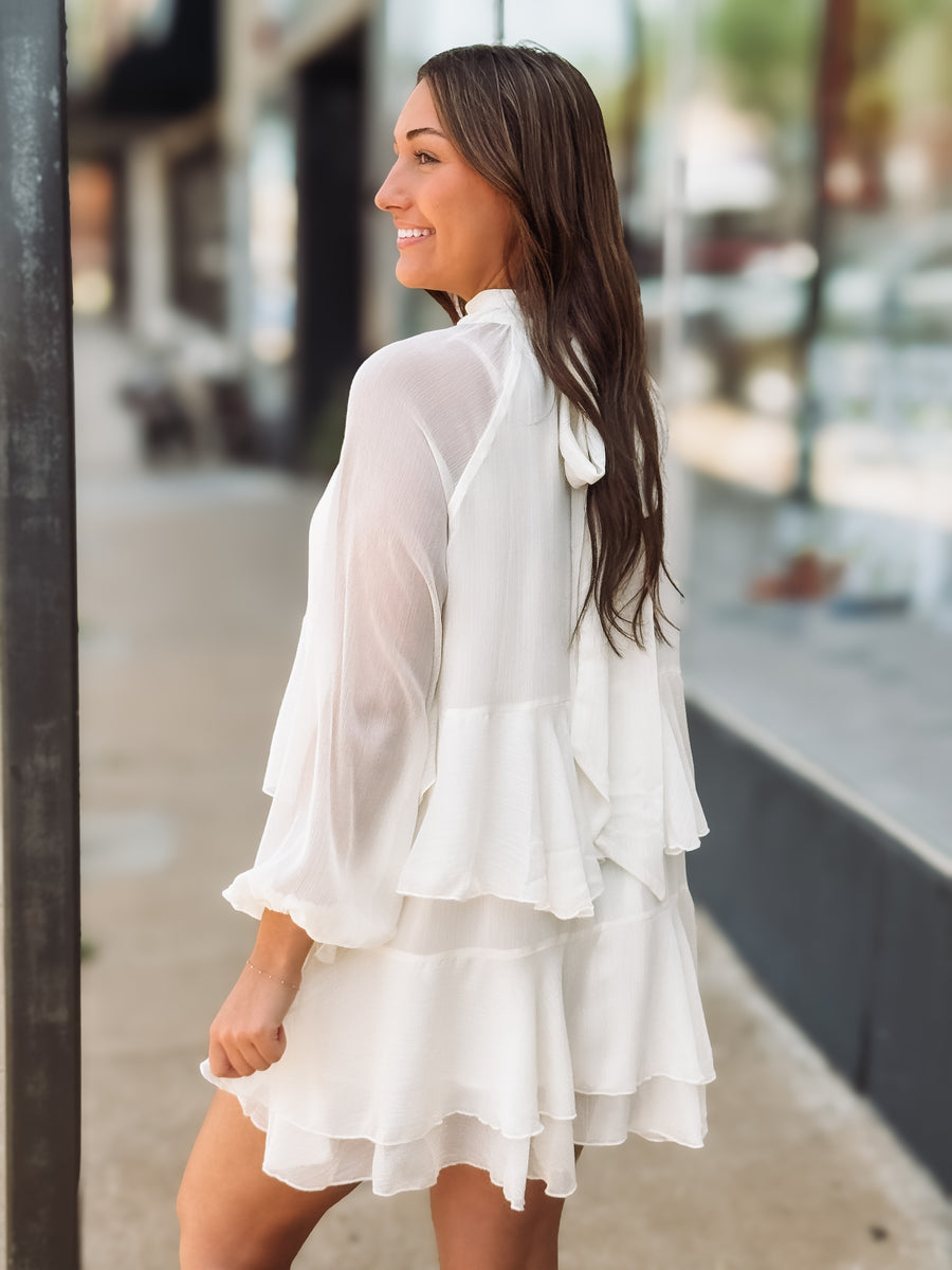Woman wearing a white dress with ruffled layers on a city street.