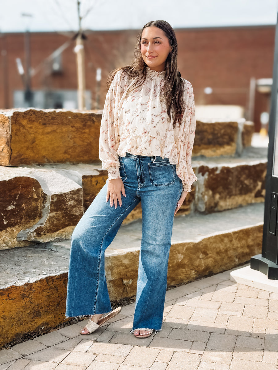 Woman wearing a floral blouse and blue jeans standing outdoors.