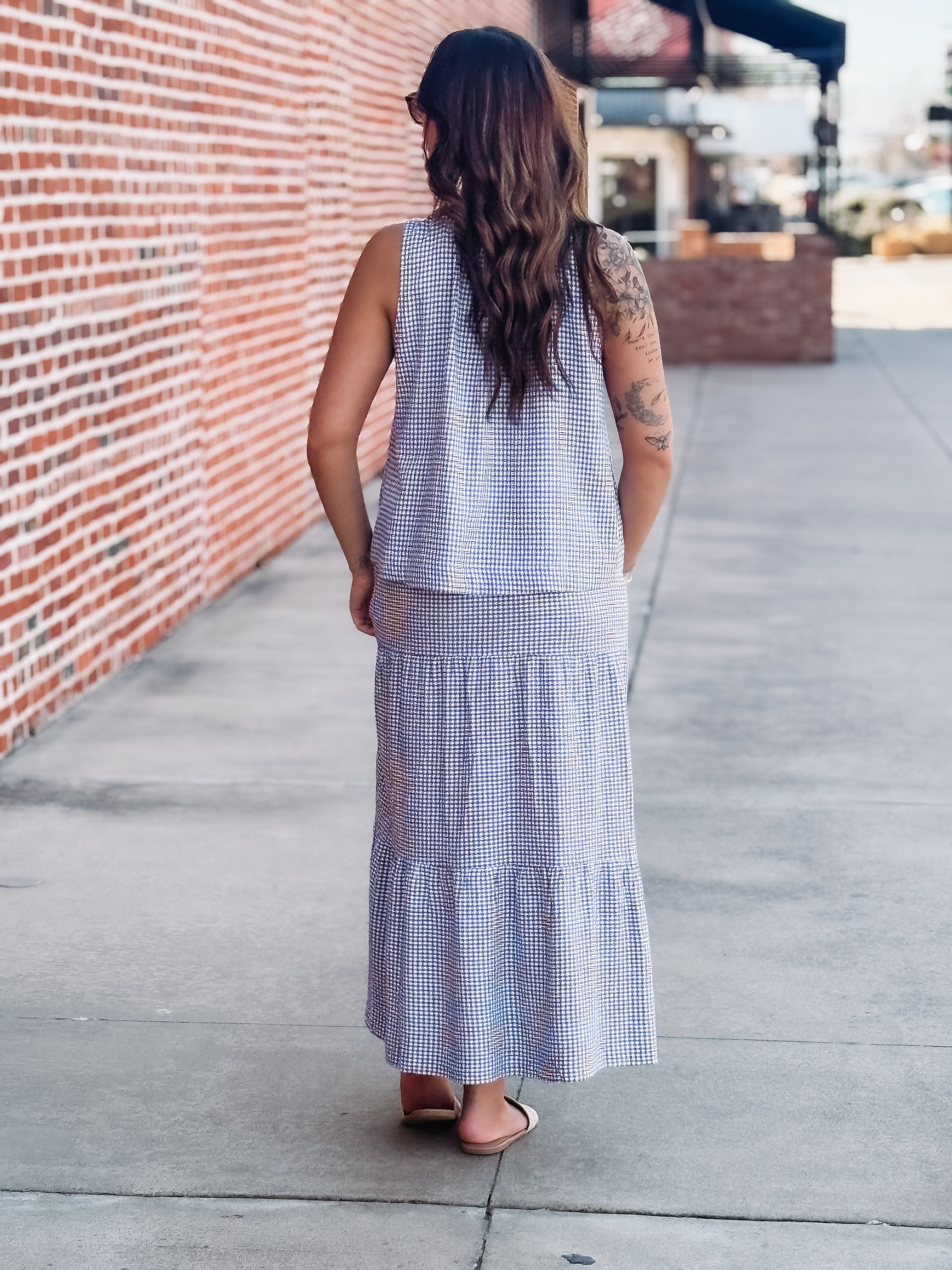 Woman wearing a checkered dress walking on a sidewalk.