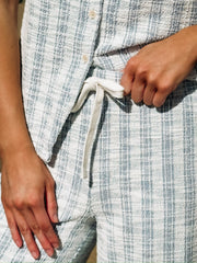 Sleeveless, textured two-piece outfit in a soft light blue and white woven fabric. The top features a round neckline, front button detailing, and a slightly relaxed, straight fit. The matching pants are high-waisted with a wide-leg silhouette
