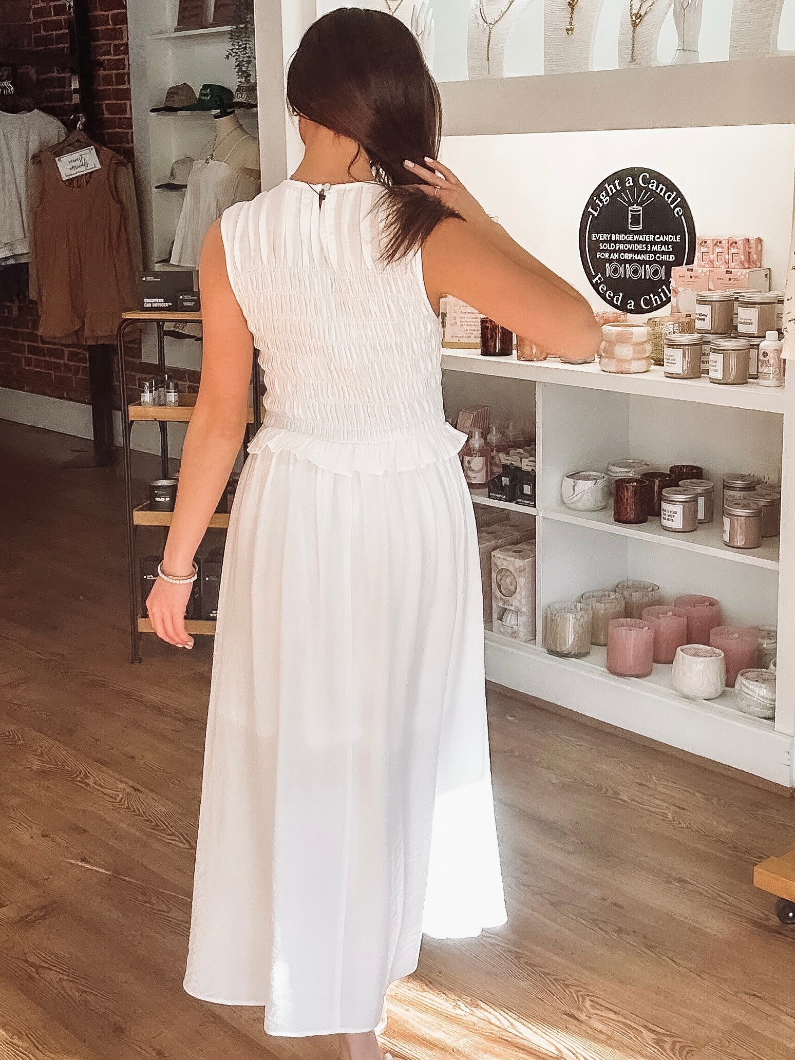 Woman in a white dress browsing items on a shelf in a store.