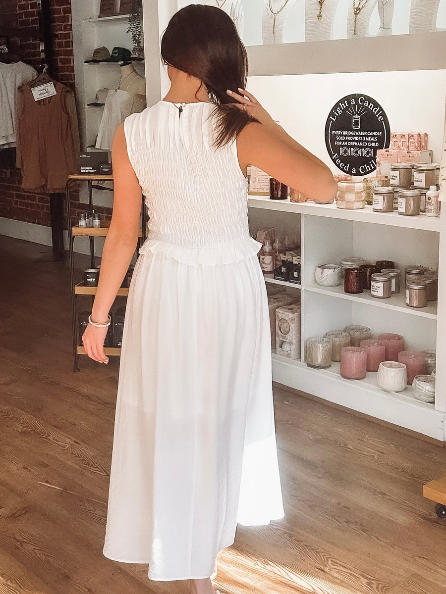 Woman in a white dress browsing items on a shelf in a store.